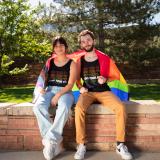 Students sitting on a wall with a pride flag.