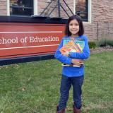 Alana Valladares poses with her books in front of the School of Education building