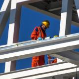 A construction worker in a helmet is seen surrounded by steel framing.
