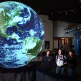 People look at an image of Earth projected on a sphere.