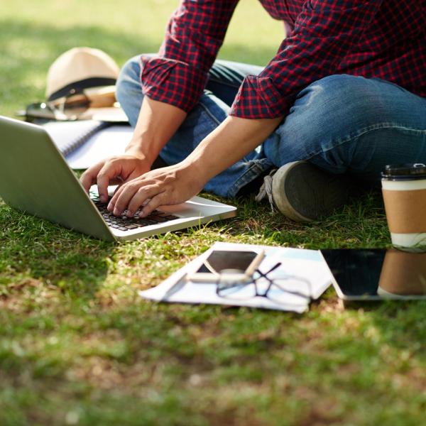student sitting in grass working on a computer