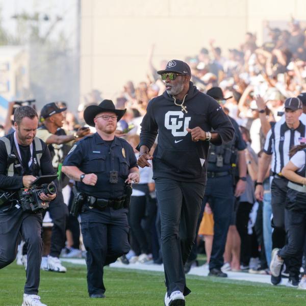 Deion Sanders (Coach Prime) runs onto the field with Chip during a football game