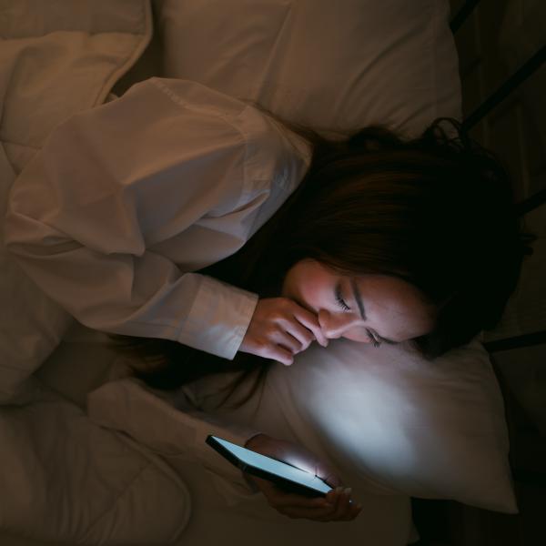 person lying in bed looking at phone