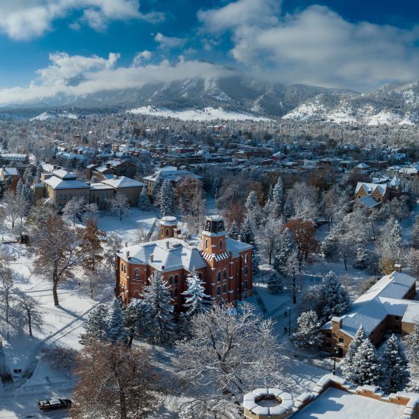 Drone shot of Old Main with the Flatirons in the background on a snowy day