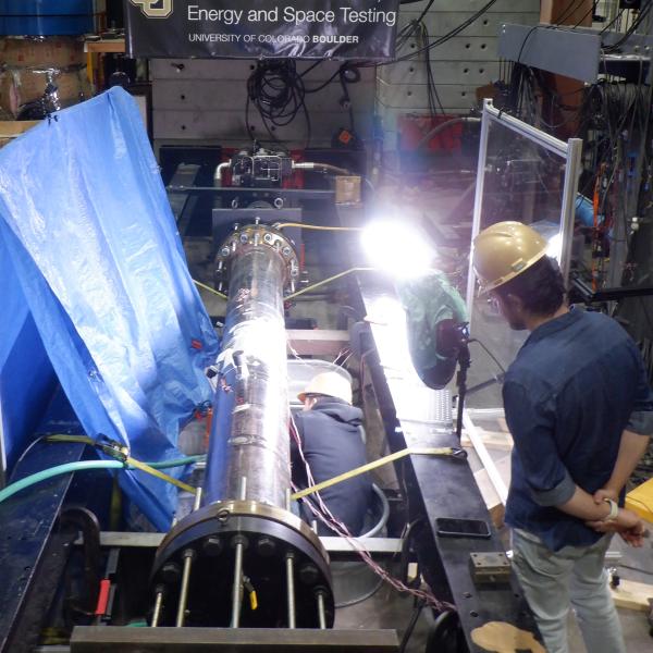 People in hard hats crouch over large pipes, appearing to repair them.