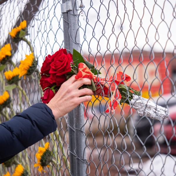 Person rests a bouquet of roses in a chainlink fence