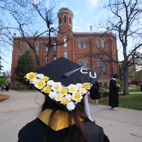 CU graduate in regalia in front of Old Main