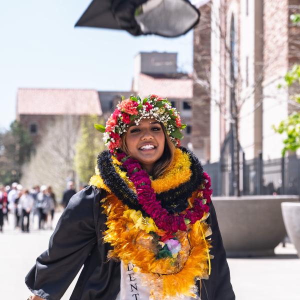 Graduate wearing leis throws cap in the air