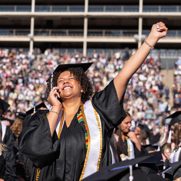Graduate with hand raised in air on Folsom Field
