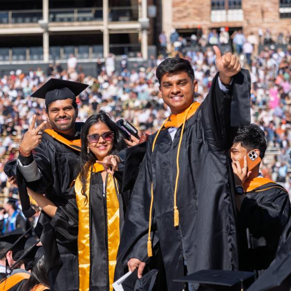 Graduates pose for a photo with hands raised on Folsom Field