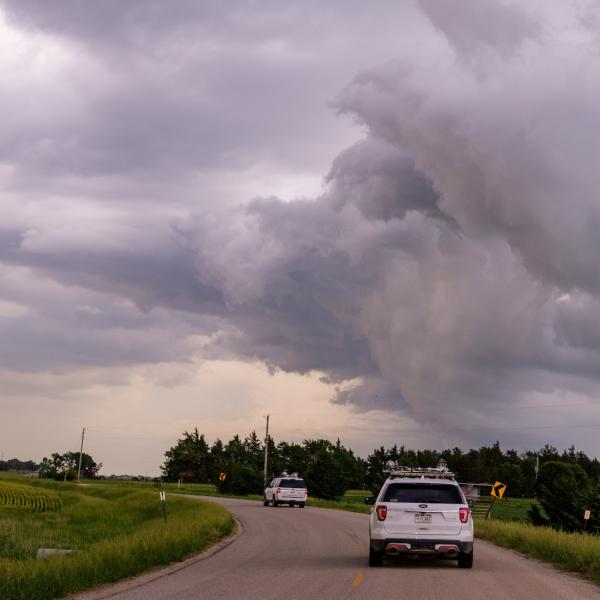 Two white SUVs drive down a single-lane highway in the country as gray storm clouds form overhead