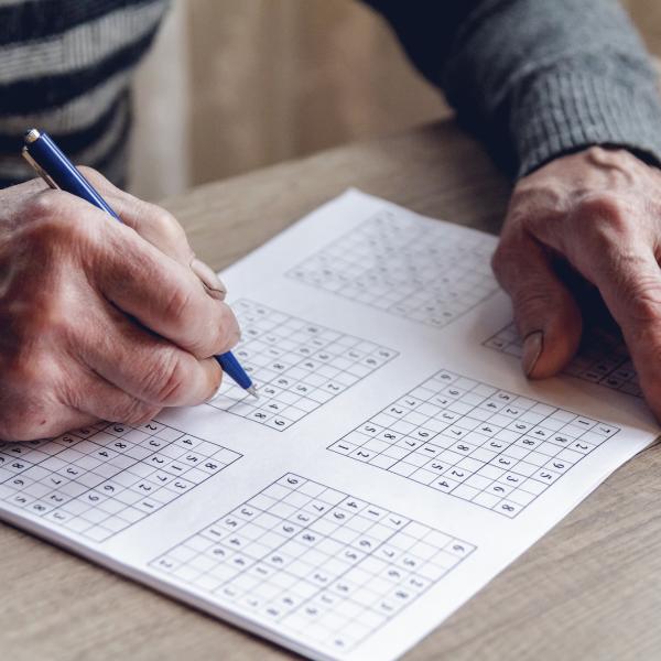 Hands filling in a sudoku grid with a pen
