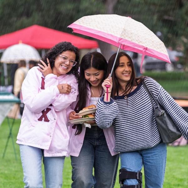 students crowd under an umbrella in the rain at CUnity Fest