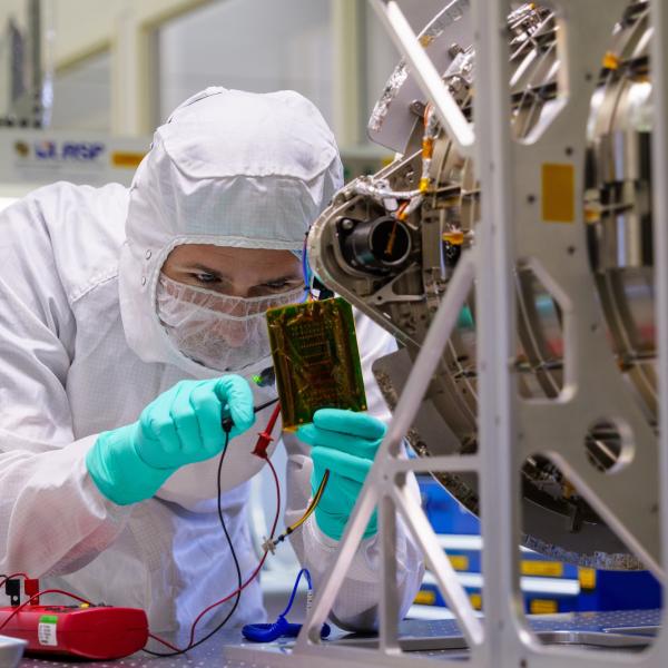 Man wearing full clean room gear works on a scientific instrument