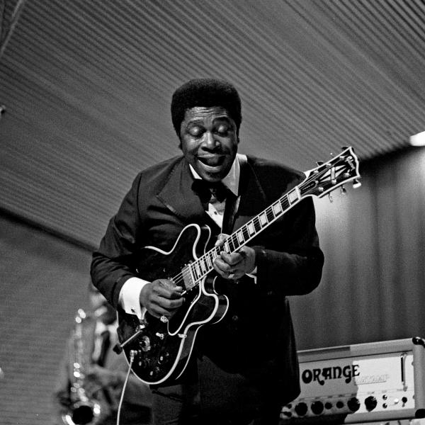 A black and white photo shows B.B. King holding an electric guitar and standing near a microphone.