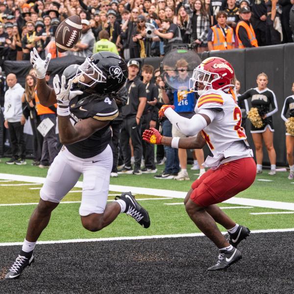Football players in opposing uniforms play on a field, with one catching a ball in his hands.