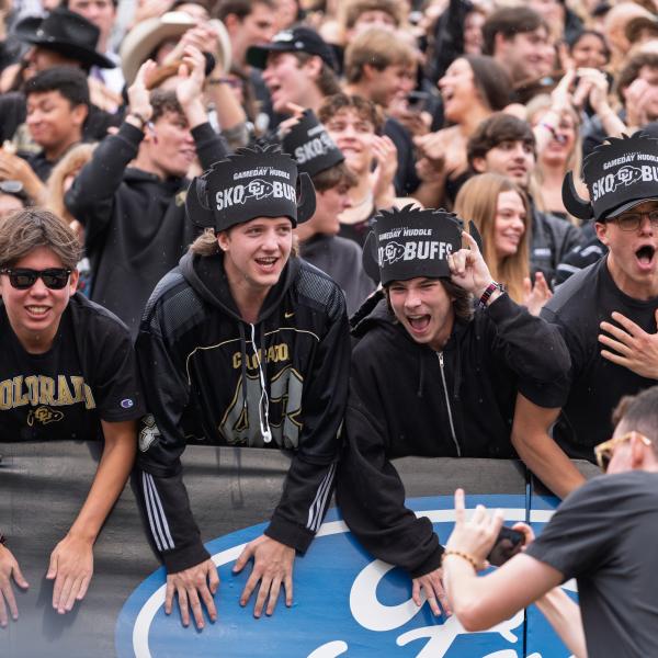 Buff fans lean over a partition, excited for the football matchup.