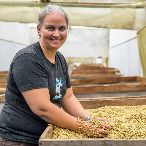Kate Fischer poses with a smile while scooping her hands into a large bin of green coffee beans.