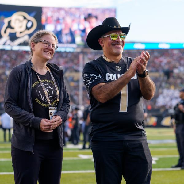 The university recognizes Katherine Stange, professor of mathematics, during pregame announcements on the field with Chancellor Justin Schwartz.