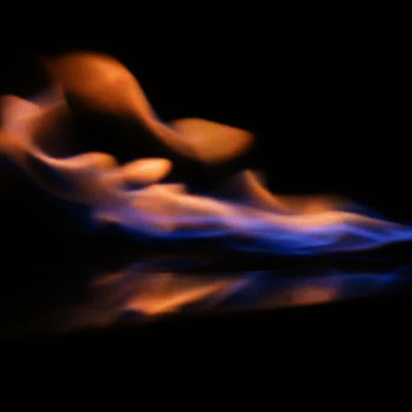 Blue and orange flame being blown by air current inside dark wind tunnel