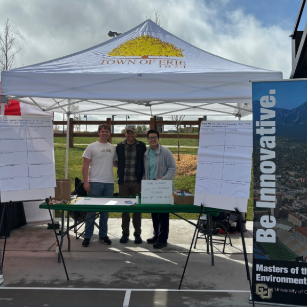 Students stand under a tent with a poster that says Be Innovative in front of them.