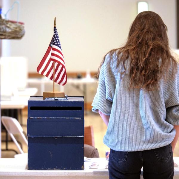 person stands next to ballot box at a campus voting center
