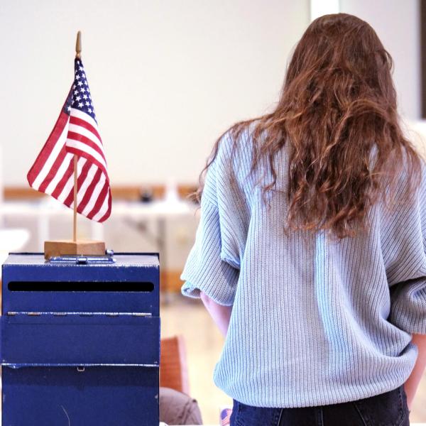 person standing next to a vote dropbox with an American flag
