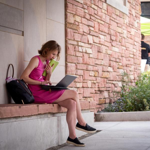 Campus community member works on laptop while sitting outside