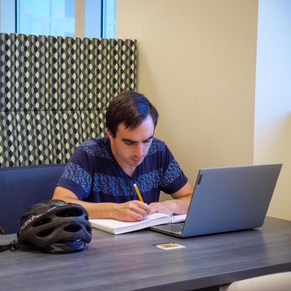 student writing in notebook with laptop opened up