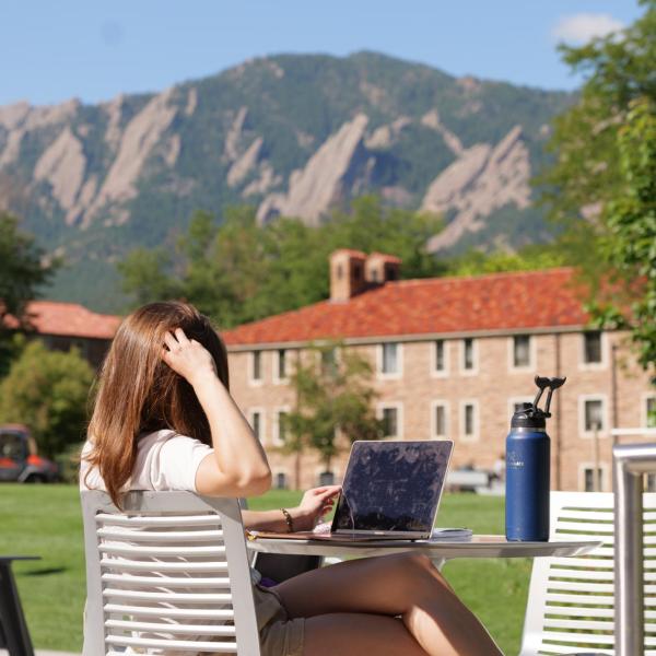 person sitting outside on campus working on laptop