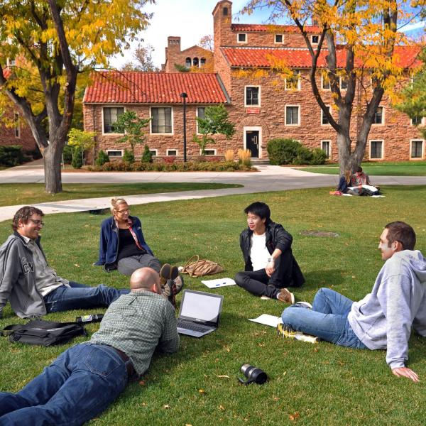 People sit in a circle on a campus lawn.