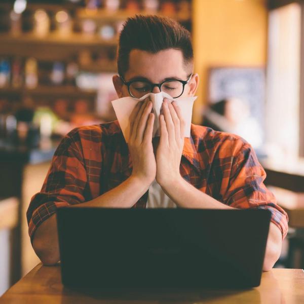 Person covering their face with a tissue while working on a laptop