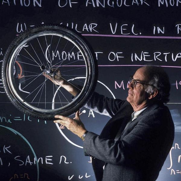 Professor Albert Bartlett holds up bicycle wheel in classroom