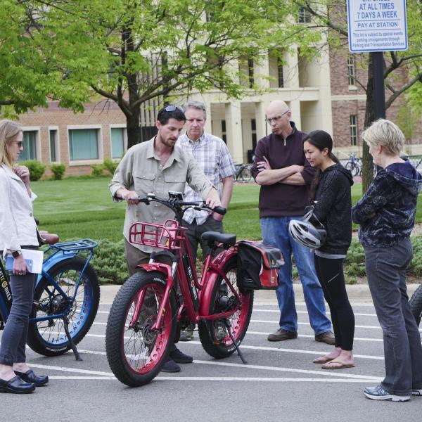 Campus community members gather around electric bikes during the 2018 Alternative Fuel Vehicle Ride-n-Drive event