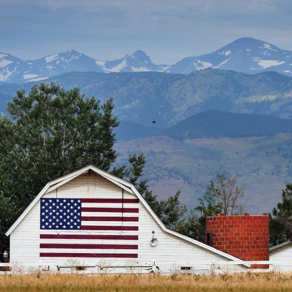 White barn with painted American flag sits in front of the Rockies
