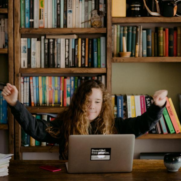 Student at computer with hands raised in celebration