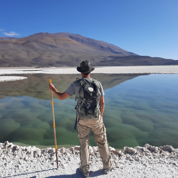 Brian Hynek holding a walking stick on the shore of a lagoon