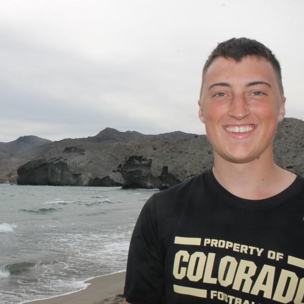 Austin Riley stands in his black CU football shirt on the beach on the coast of Spain.