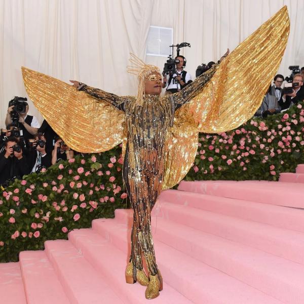 Bill Porter appears at the Met Gala in entirely gold beaded attire, including large wings extending beyond his hands.