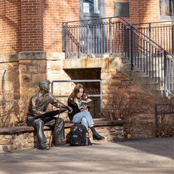 student reading on campus next to Robert Frost statue
