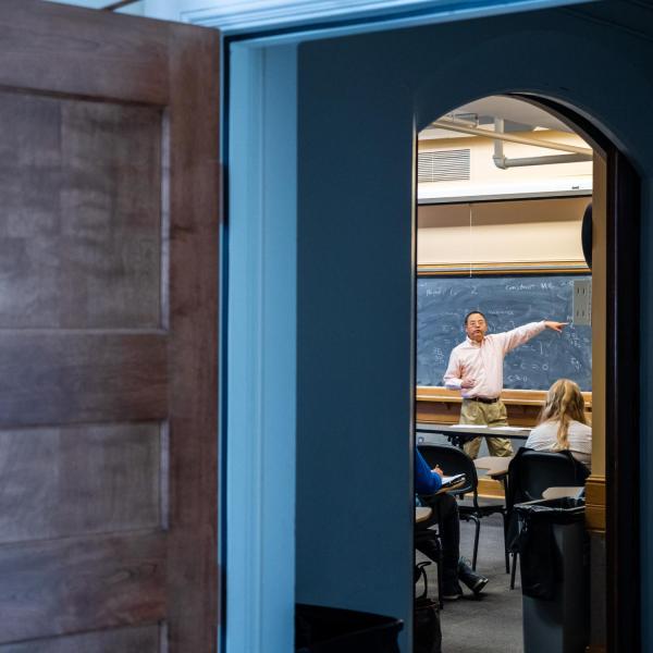 An instructor points to a black board in front of a class of students.