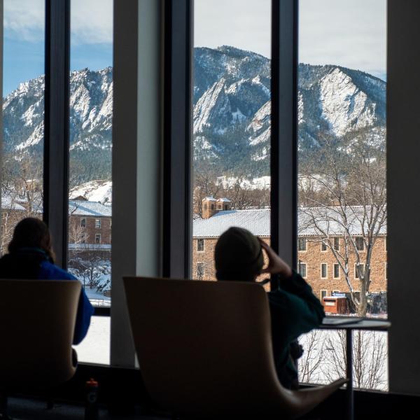 Students sitting in chairs looking through a window at snow-covered mountains