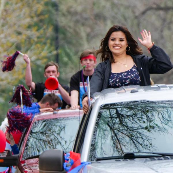 Students stick their heads out of car sunroofs as part of a car parade.