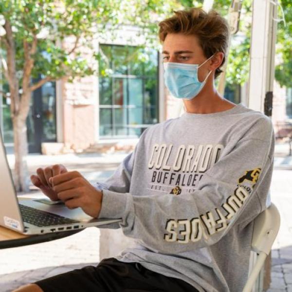 Man in face covering working on a computer.