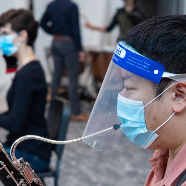 Student plays a musical instrument with a mask and a face shield on.