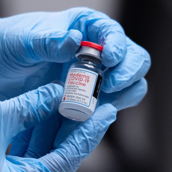 Gloved hands hold a vaccine vial