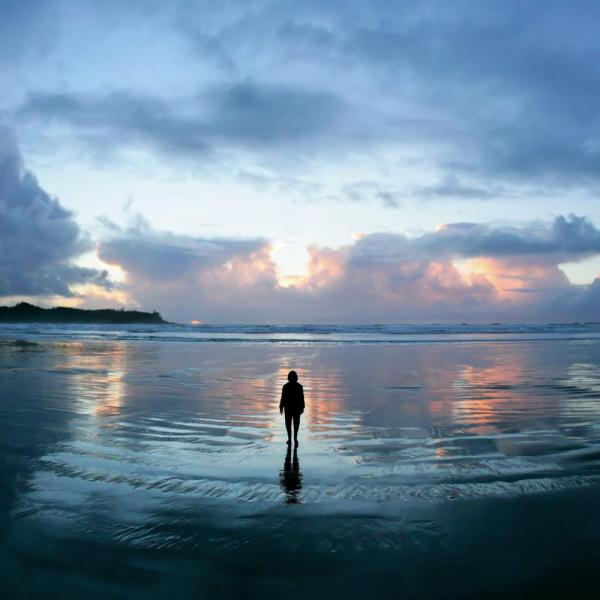 Silhouette of person walking toward the ocean at sunset