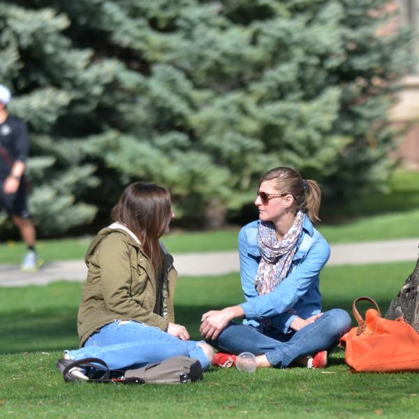 Two students chat sitting on lawn