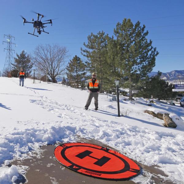 Members of the GEER team watch a drone take off from a snowy driveway