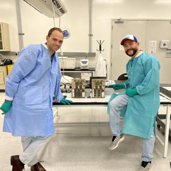 Tobias Niederwieser and Luis Zea pose by two cases on a table in a lab